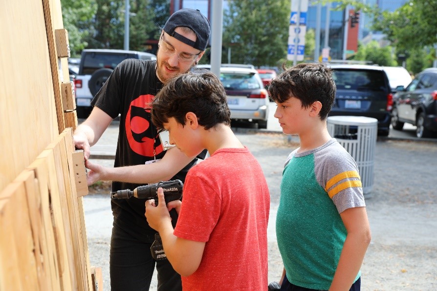 Photo of Weston Hambleton showing two boys how to use a drill