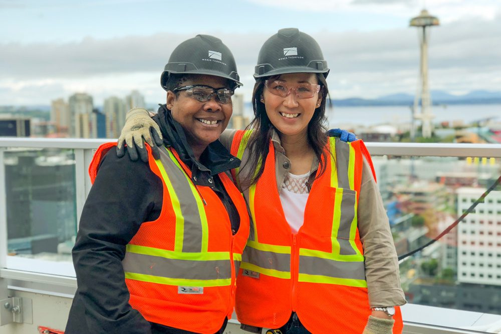 Photo of Susan Frieson and Lisa Kim Bartin on the rooftop of Ascent in South Lake Union with the Space Needle in the background.