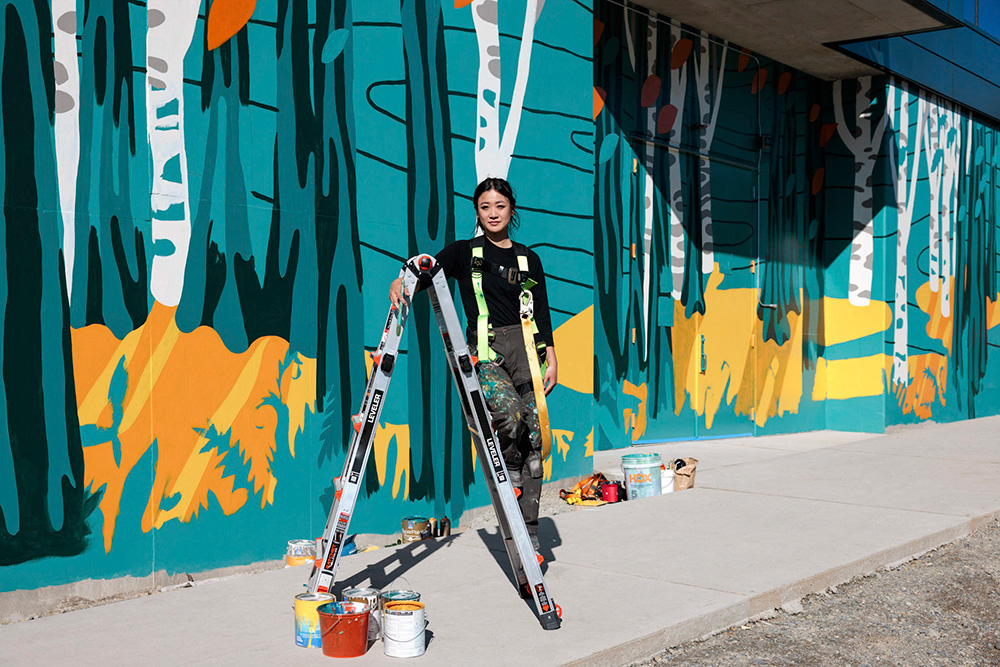 Photo of Artist Tori Shao standing in front of the Northlake Commons mural