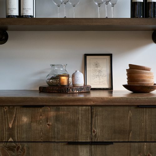 photo of a decorated wood wine cabinet with wine bottles, a low lit candle, and wooden bowls