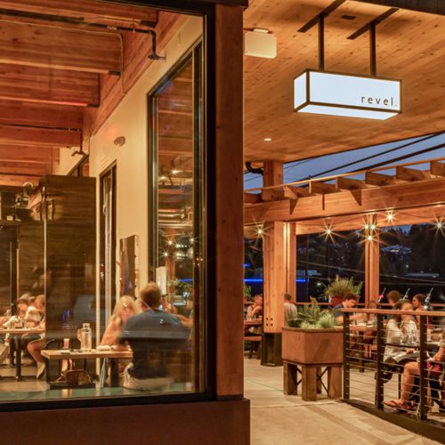 photo of the exterior of revel restaurant in seattle at dusk with people sitting outside on the patio and people inside dining through the window