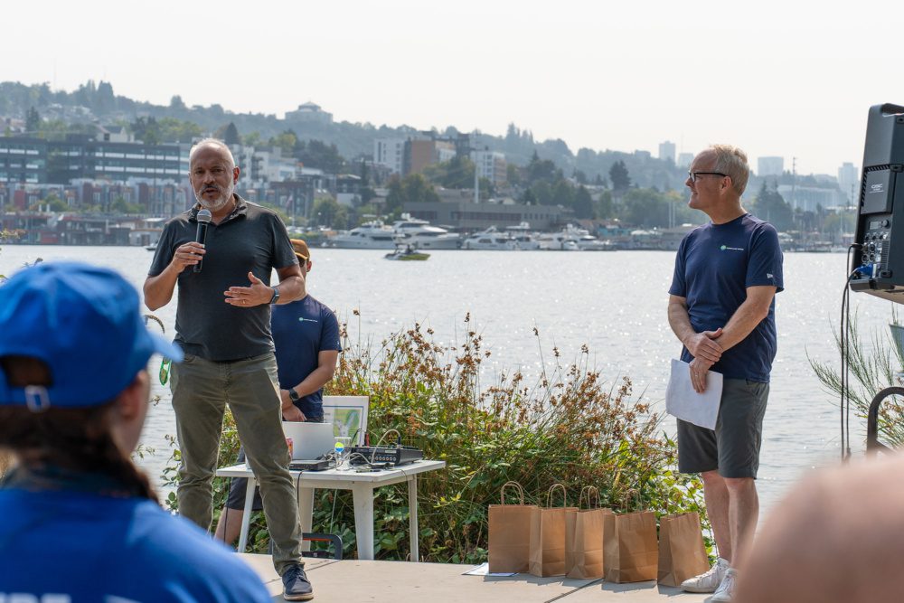 photo of Mark Grey and King County Council member Jorge Barón talking on stage with lake union in the background