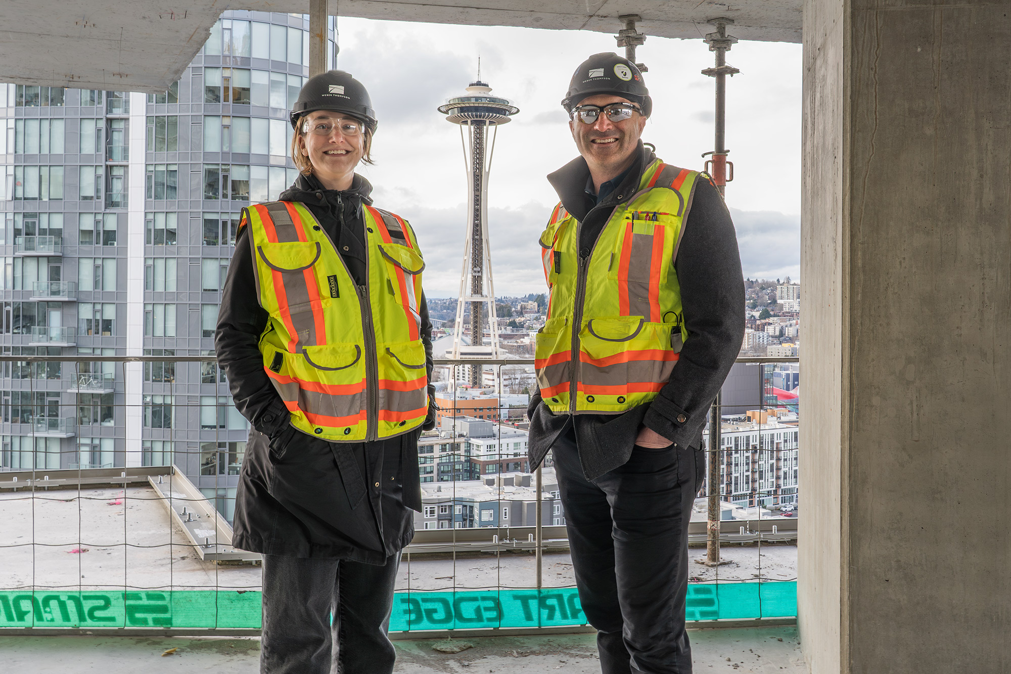 two weber thompson employees standing at a construction site with the space needle in the background