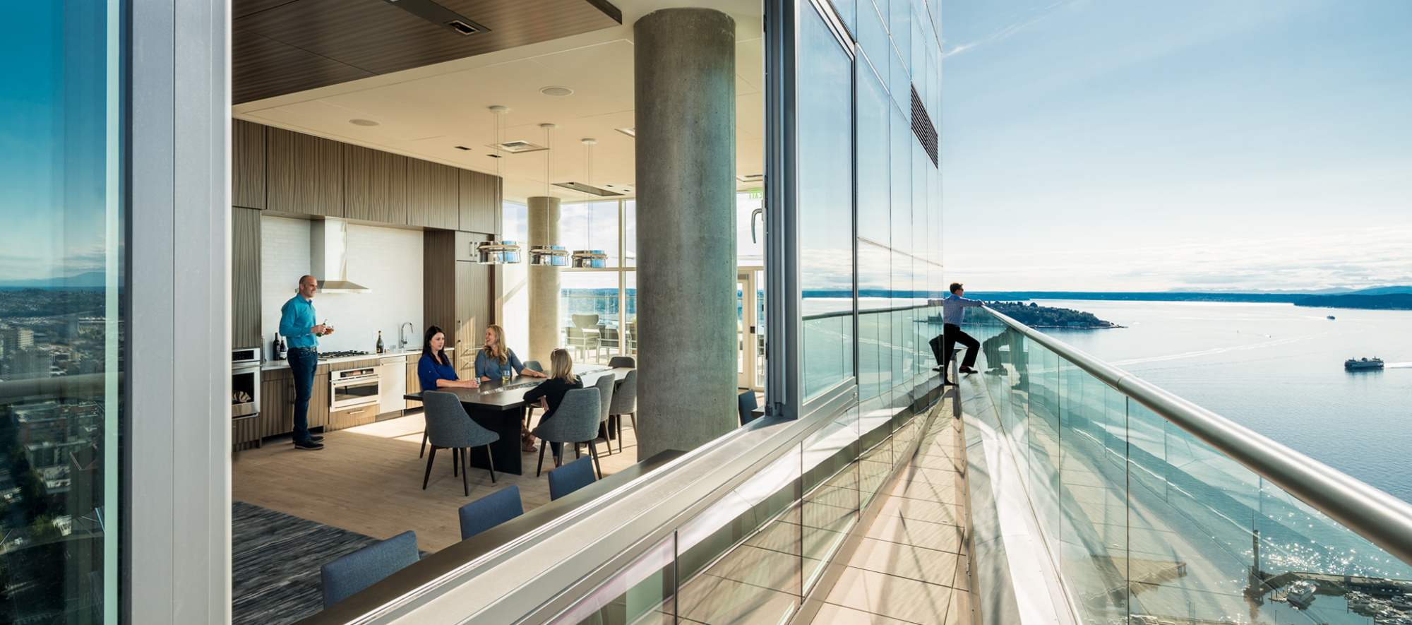 photo of the roof deck at helios overlooking the puget sound with people sitting inside and someone looking over the balcony