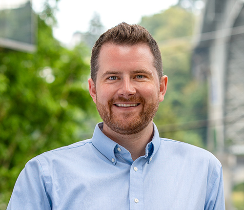Portrait of Dan Fohn taken outdoors with green foliage in the background